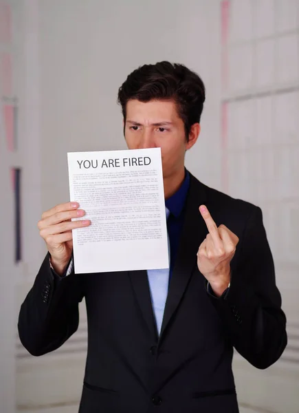 Gros plan d'un homme d'affaires en colère portant un costume et tenant une feuille de papier sur laquelle vous avez tiré du texte, faisant un signe du majeur, dans un arrière-plan flou — Photo