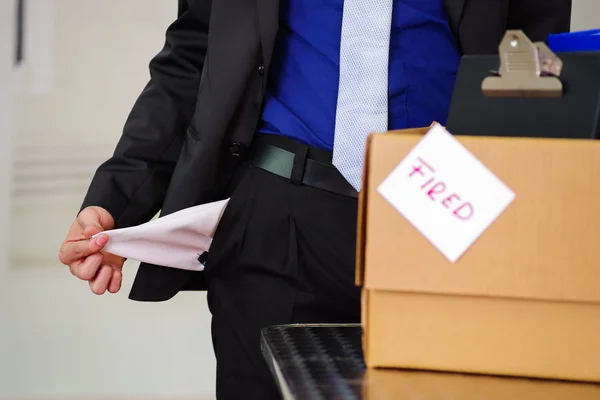 Close up de homem vestindo um terno segurando seus bolsos vazios com uma caixa de seus pertences depois de ser demitido de seu trabalho em um fundo turvo — Fotografia de Stock