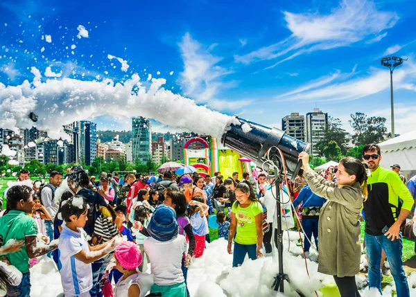 QUITO, ECUADOR- NOVEMBRE, 28, 2017: Veduta esterna della donna con macchina della schiuma e gruppo di bambini che si divertono e ballano ad una festa in schiuma al festival di Quito — Foto Stock