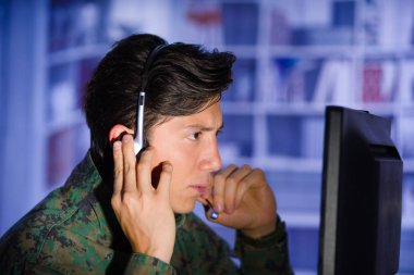 Yakışıklı asker kulaklık bir eliyle onun bilgisayar önemli bilgileri izlemek ve bulanık arka planda, profil resmi bir tavsiyede askeri üniforması portresi