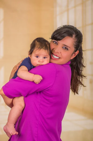 Primer plano de la joven madre sostiene a su pequeño bebé, mamá con una blusa púrpura y ropa azul bebé, en un fondo borroso — Foto de Stock