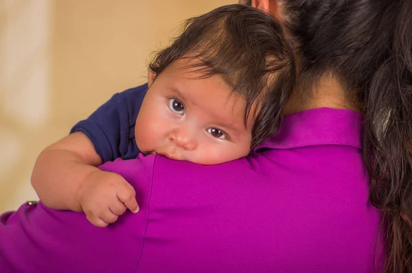 Primer plano de la joven madre sostiene a su pequeño bebé, mamá con una blusa púrpura y ropa azul bebé, en un fondo borroso — Foto de Stock