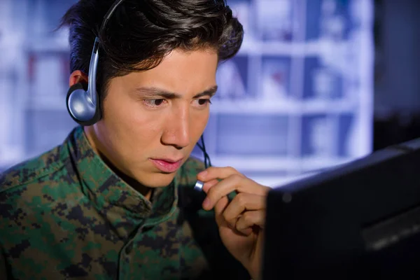 Portrait of soldier wearing a military uniform, operating at his computer and talking through his headphones to give an advice