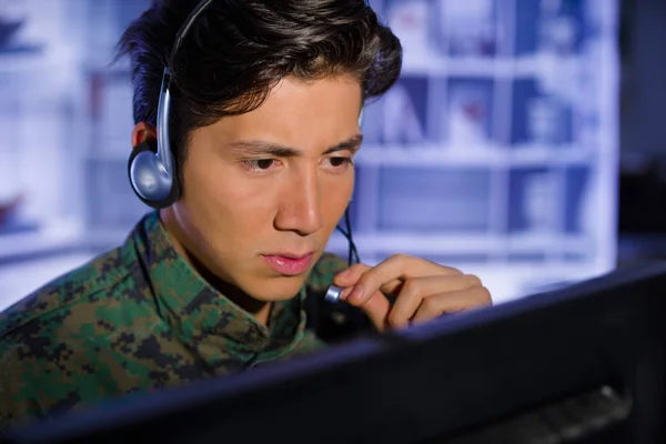 Retrato del soldado vestido con uniforme militar, operando en su computadora y hablando a través de sus auriculares durante una operación militar, en un fondo borroso —  Fotos de Stock