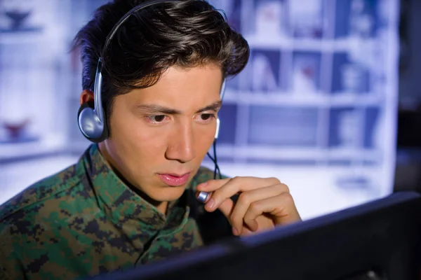 Retrato del soldado vestido con uniforme militar, operando en su computadora y hablando a través de sus auriculares durante una operación militar, en un fondo borroso — Foto de Stock