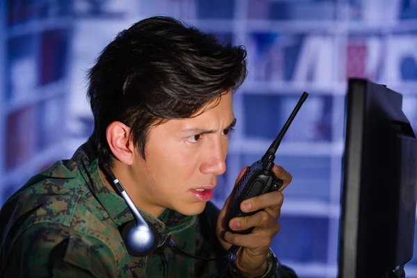 Retrato del joven soldado con uniforme militar, operador militar de drones mirando su computadora y usando una radio para dar un consejo, con auriculares alrededor de su cuello — Foto de Stock