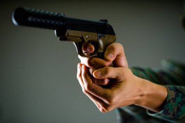 İki elinle silah gri arka planda bir askerin kapalı görünüm