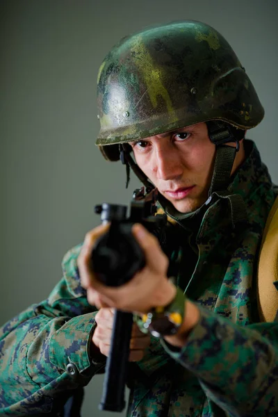 Ritratto di bel giovane soldato che tiene tra le mani un fucile, indossa un'uniforme militare, messa a fuoco selettiva su sfondo grigio — Foto Stock