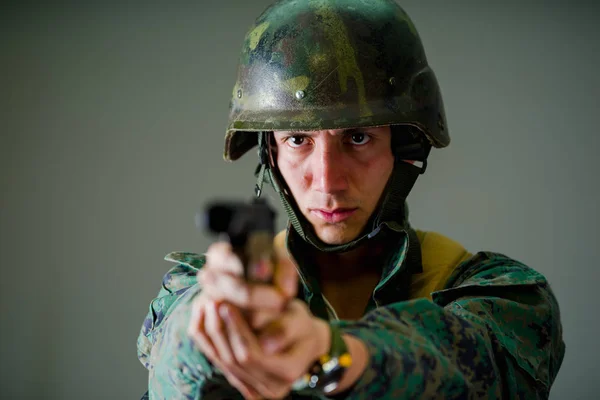 Portret młodego żołnierza, wskazując broń w szarym tle — Zdjęcie stockowe