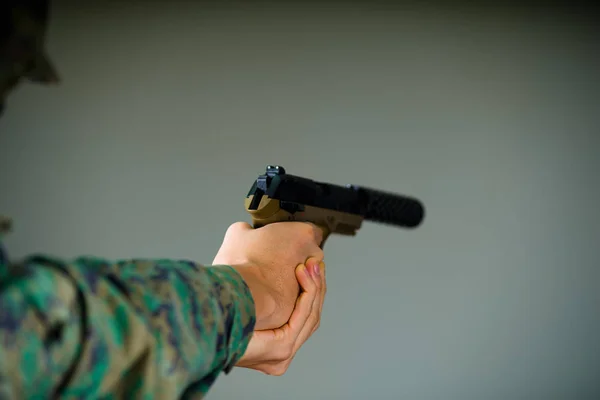 Vista interior de un soldado sosteniendo con ambas manos una pistola en fondo gris —  Fotos de Stock