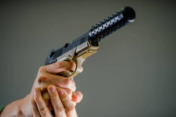 Close-up de um soldado segurando com ambas as mãos uma arma pesada em fundo cinza — Fotografia de Stock