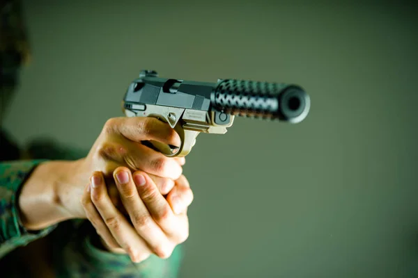 Close-up de um soldado segurando com ambas as mãos uma arma pesada em fundo cinza — Fotografia de Stock