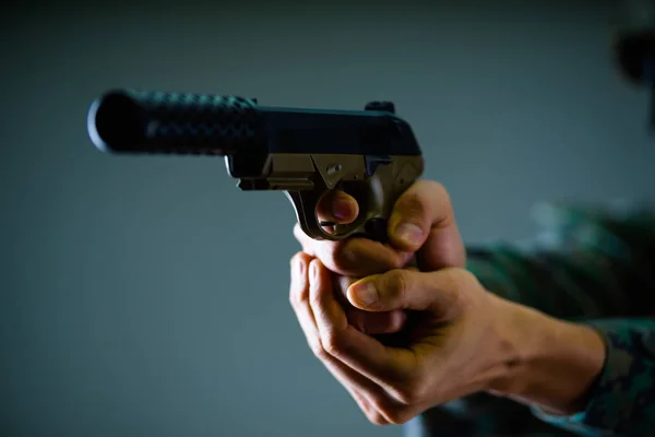 Κοντινό πλάνο ενός στρατιώτη κρατώντας με τα δύο χέρια ένα βαρύ όπλο σε γκρίζο φόντο — Φωτογραφία Αρχείου