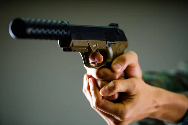 Close-up de um soldado segurando com ambas as mãos uma arma pesada em fundo cinza — Fotografia de Stock