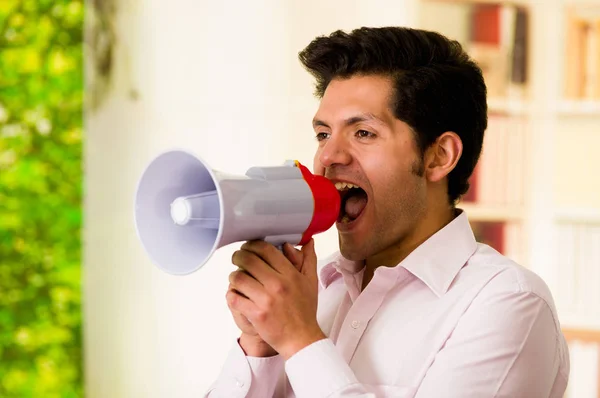 Nahaufnahme eines jungen Mannes, der mit einem Megafon ruft, dicht vor seinem Mund in einem verschwommenen Hintergrund — Stockfoto