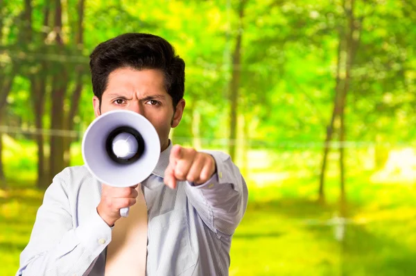 Retrato de un hombre guapo gritando con un megáfono mientras señala delante de él su mano, en un fondo verde borroso — Foto de Stock