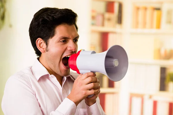 Close up of young man shouting with a megaphone, close to his mouth in a blurred background — Stock Photo, Image