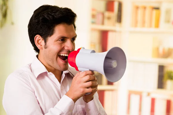 Portrait of a smiling handsome man talking with a megaphone in a blurred background — Stock Photo, Image