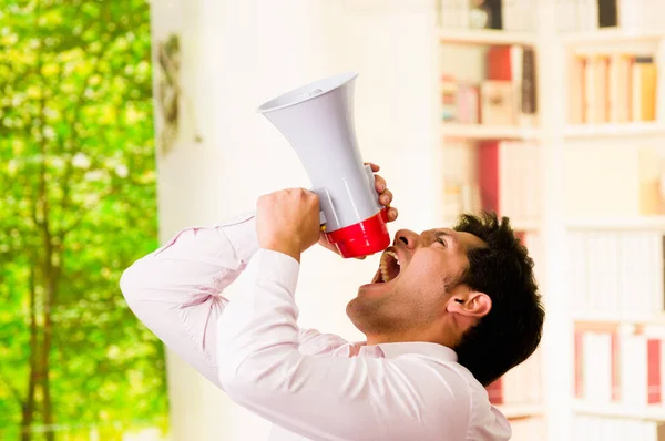 Acercamiento de un hombre guapo gritando con un megáfono, apuntando al cielo en un fondo borroso — Foto de Stock