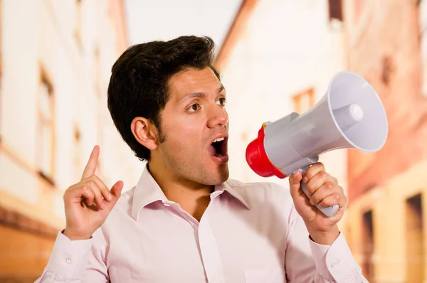 Acercamiento de un hombre guapo gritando con un megáfono, haciendo una señal con la mano en un fondo borroso — Foto de Stock
