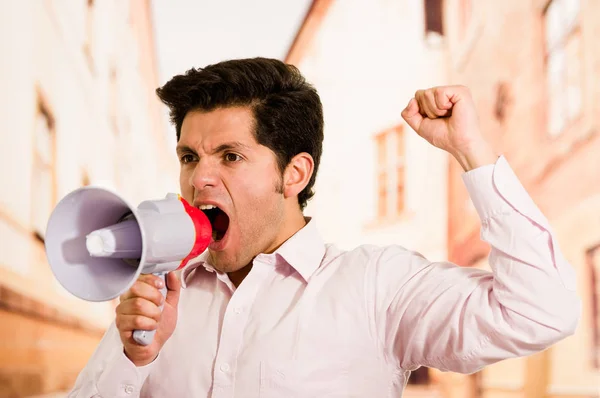 Zblízka mladý pohledný muž křičí s megafon, s pěstí na vzduchu burred pozadí — Stock fotografie