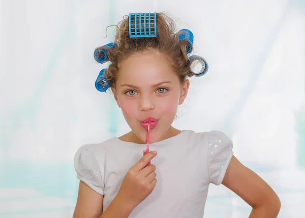 Little girl painting lips while wearing hair-rollers and bathrobe