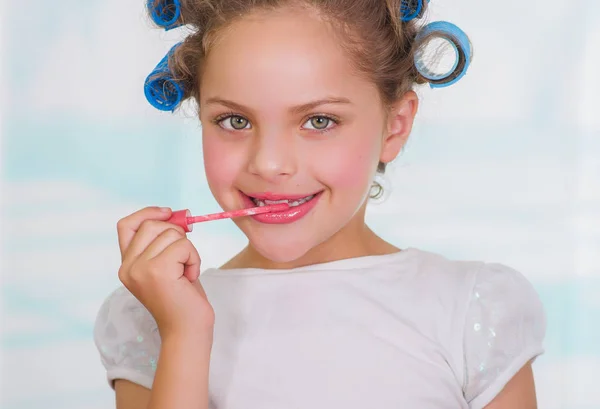 Portrait of little girl painting lips while wearing hair-rollers and bathrobe — Stock Photo, Image