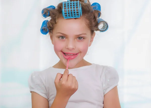 Portrait of little girl painting lips while wearing hair-rollers and bathrobe — Stock Photo, Image