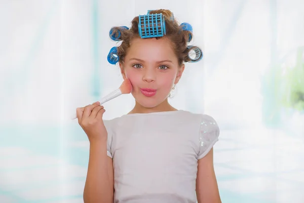 Little girl using a brush to make up while wearing hair-rollers and bathrobe — Stock Photo, Image