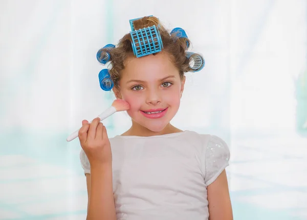 Menina usando um pincel para fazer as pazes enquanto vestindo rolos de cabelo e roupão — Fotografia de Stock