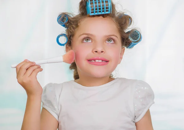Küçük kız yapmak için bir fırça kullanarak bulanık bir arka planda saç-silindirler ve bornoz giyen süre yukarı — Stok fotoğraf