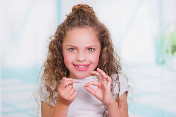 Portrait of beautiful curly little girl painting her nails, wearing a white blouse in a blurred background — Stock Photo, Image