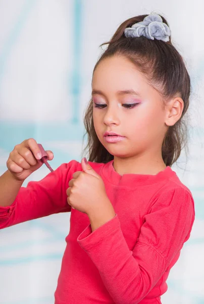 Ritratto di bella bambina che si dipinge le unghie, indossando una camicetta rossa su sfondo sfocato — Foto Stock