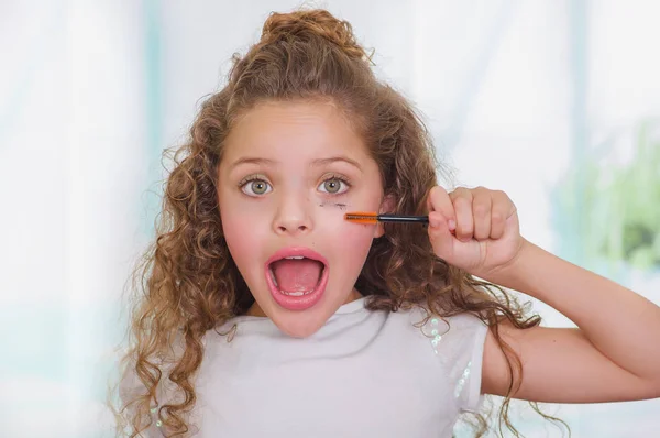 Close up of surprised little girl using wrong an eye mascara in her face in a blurred background — Stock Photo, Image