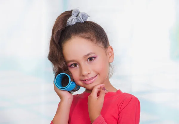 Little beautiful girl wearing hair-rollers and red blouse in a blurred background — Stock Photo, Image