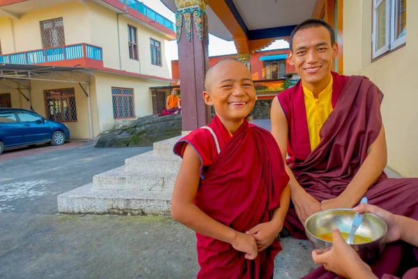 POKHARA, NEPAL - 06 DE OCTUBRE DE 2017: Adolescente monje budista no identificado sosteniendo en su mano un cuenco metálico con sopa y hablando con sus amigos al aire libre en el asentamiento de refugiados Tashi en — Foto de Stock