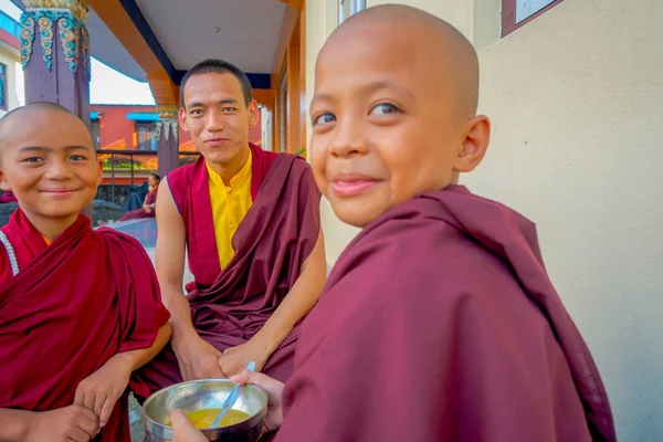POKHARA, NEPAL - 06 DE OCTUBRE DE 2017: Adolescente monje budista no identificado sosteniendo en su mano un cuenco metálico con sopa y hablando con sus amigos al aire libre en el asentamiento de refugiados Tashi en — Foto de Stock