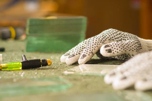 Primeros planos con guantes de trabajo blancos que sostienen el borde de la mesa, herramienta de grabado de corte portátil para vidrio que yace en frente —  Fotos de Stock