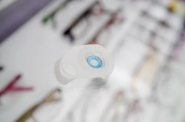 Close up de uma lente de contato azul, dentro da óptica sobre uma vitrine em um fundo embaçado — Fotografia de Stock