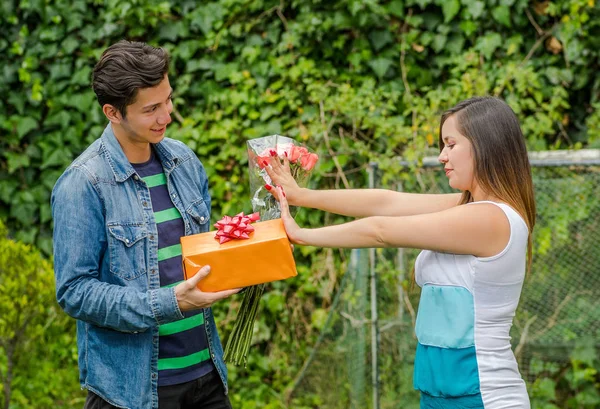 Primer plano de hombre sonriente y feliz sosteniendo un regalo y flores con su novia estirando ambos brazos ignorándolo, concepto de zona de amigos —  Fotos de Stock