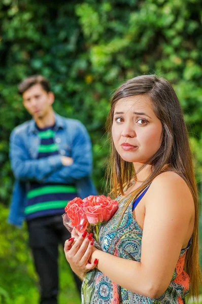 Close up of sad woman holding flowers in her hands, with her endless love man behind. Valentines Day concept or friend zone concept — Stock Photo, Image