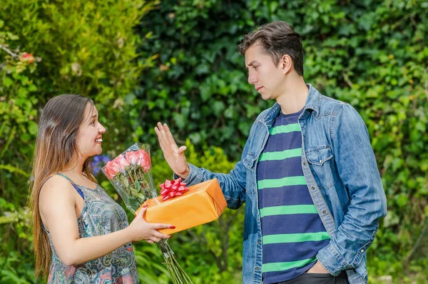 Close up of happy woman holding a gift and flowers looking at his crush and boy stretching his arm ignoring her, friend zone concept — Stock Photo, Image