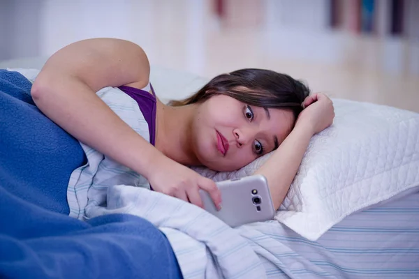 关闭一个年轻的美丽的女人患有失眠, 并使用她的手机在床上 — 图库照片