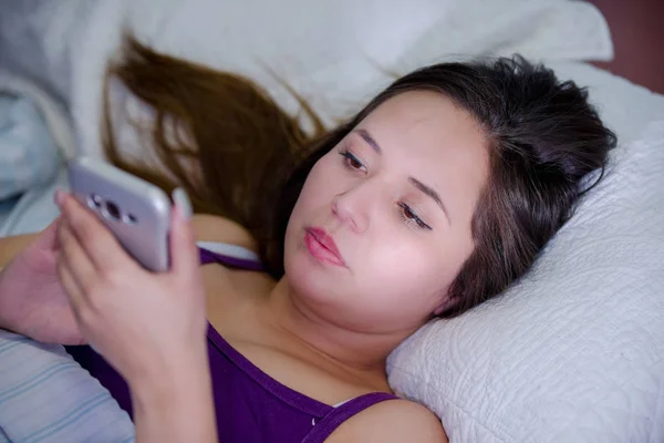 Uykusuzluk acı ve yatakta cep telefonunu kullanarak genç bir kadın portresi — Stok fotoğraf