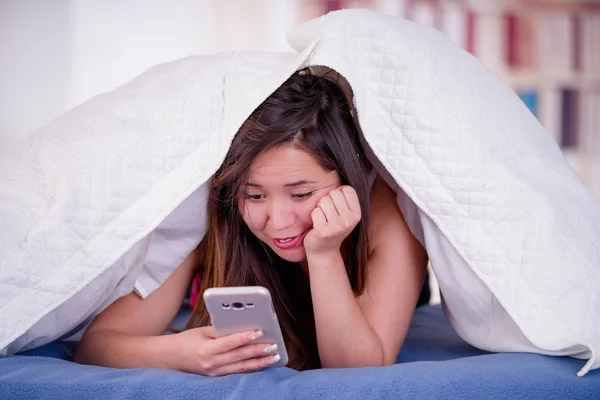 Gros plan de la femme avec sa tête sous son oreiller en utilisant son téléphone portable, essayant de dormir la nuit, concept d'insomnie — Photo