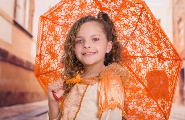 Güzel sömürge kostüm giyen ve bulanık bir arka planda turuncu bir şemsiye tutan küçük kızın yakın çekim — Stok fotoğraf