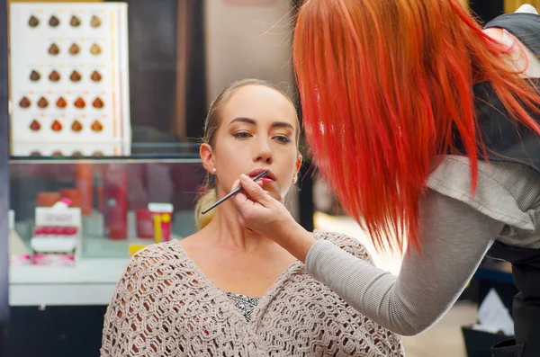 Primer plano de la hermosa joven maquillándose. La artista se aplica lápiz labial en la boca, en un fondo borroso — Foto de Stock