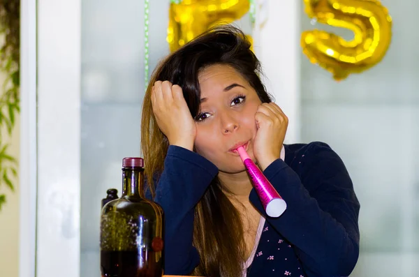 Mujer joven con un silbato en la boca, y una botella de alcohol en la mesa, concepto de resaca —  Fotos de Stock