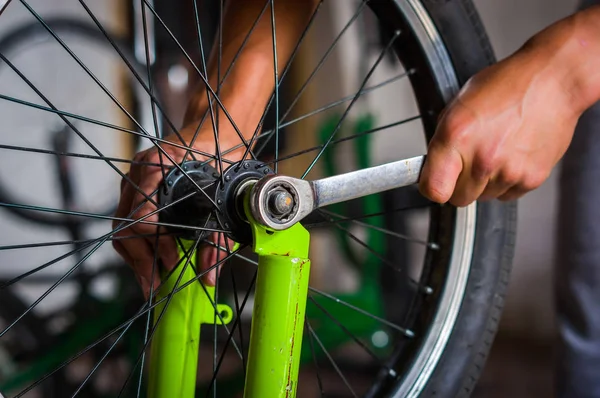 Primer plano del mecánico de bicicletas en un taller en el proceso de reparación de la rueda con una llave inglesa —  Fotos de Stock