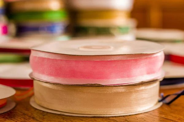 Nahaufnahme von Rollen aus buntem rosa und weißem Stoffband, über einem Holztisch vor verschwommenem Hintergrund — Stockfoto